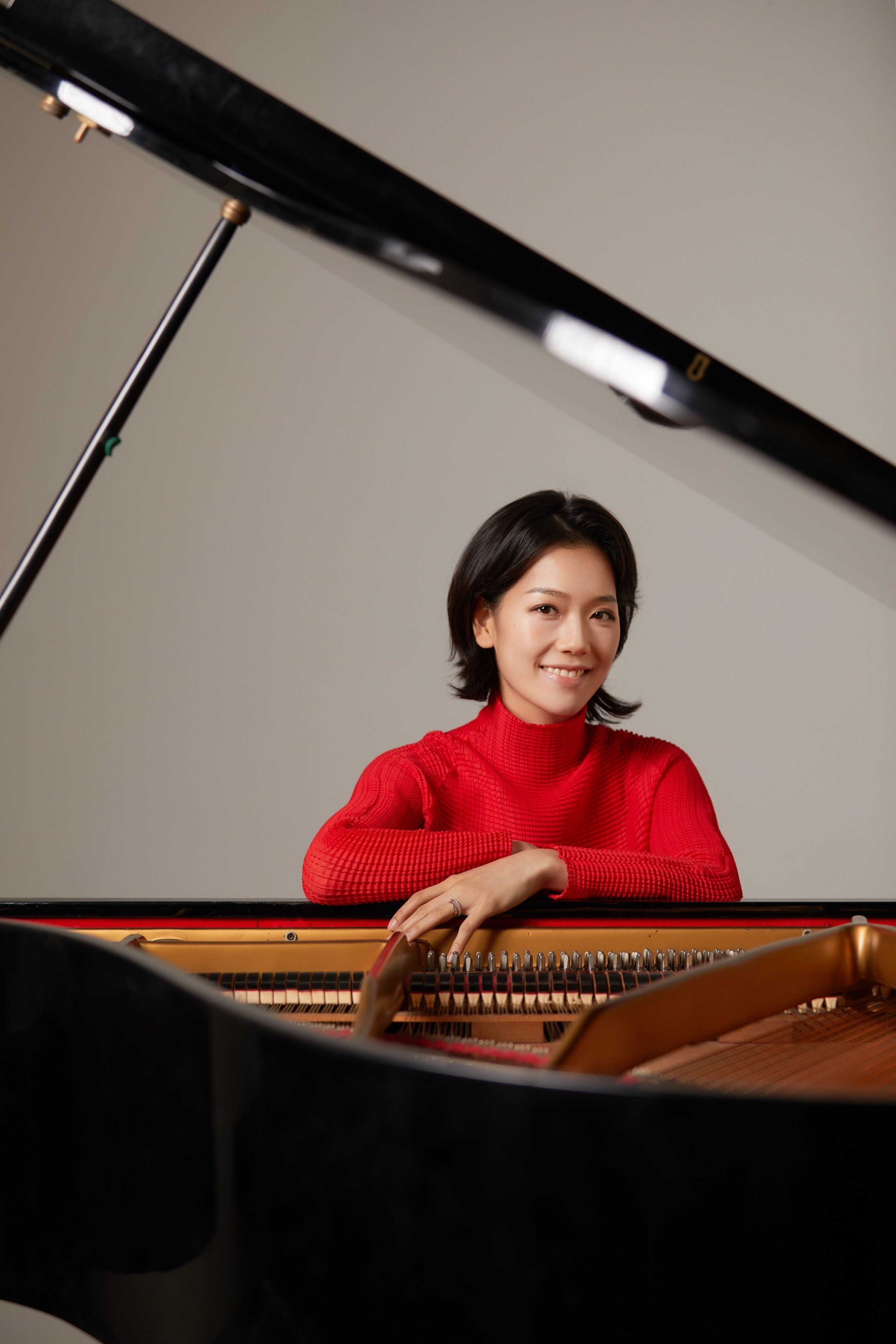 Photo of Suejin Jung resting on a grand piano wearing a red turtle neck
